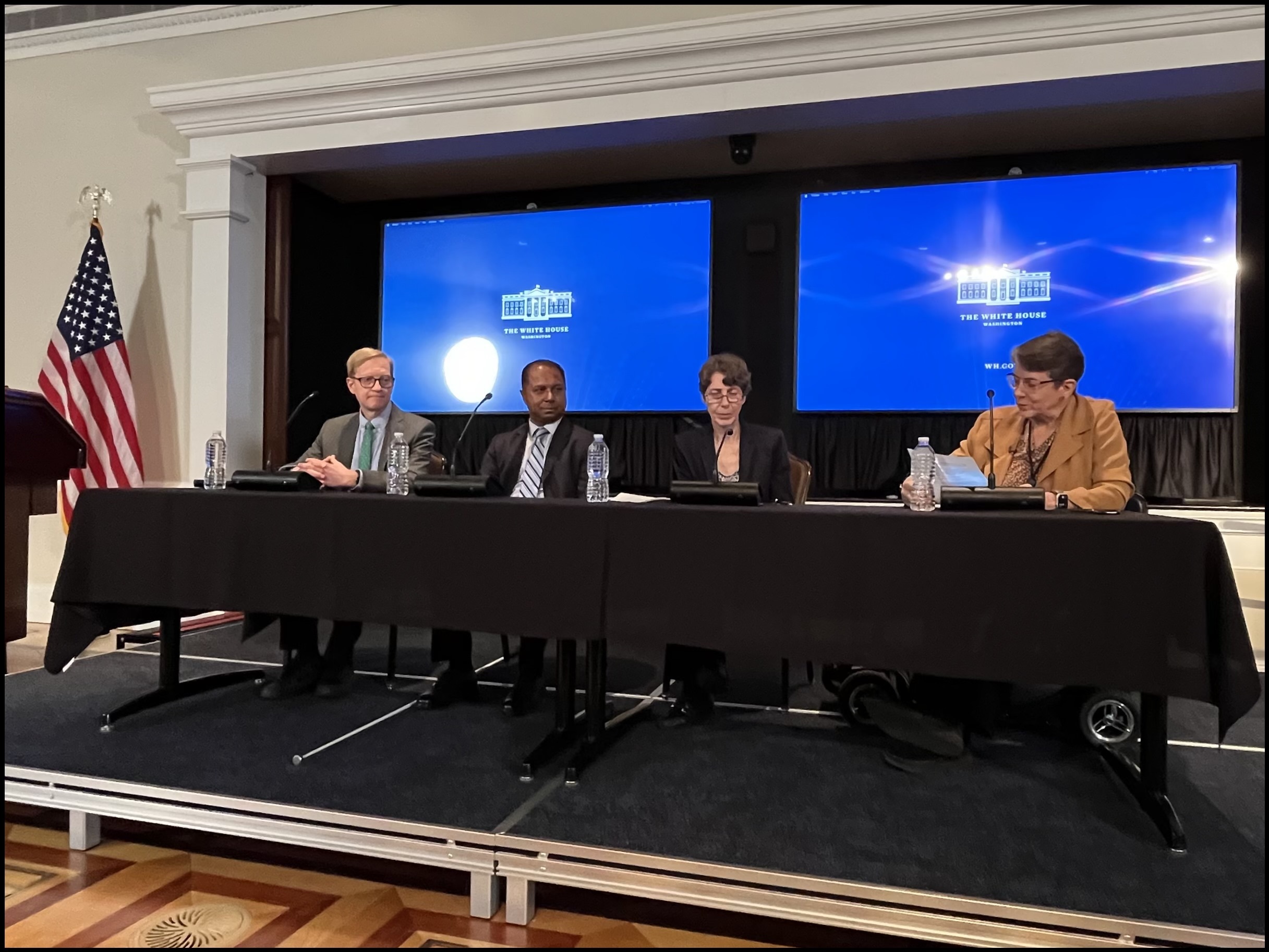 Jennifer Mathis, DOJ; Sam Bagenstos, HHS; Sachin Pavithran; and Judy Brewer from the White House Office of Science and Technology Policy sit at a table during a panel. Behind them are two screens displaying the White House logo, and to the left is the U.S. flag.