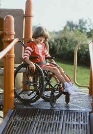 photo of a girl using a wheelchair at the top of play structure's ramp 