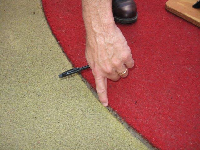 A researcher inserts his index finger into the one inch gap between the seam of the yellow and red carpets.