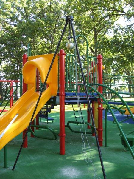 A TRIAX tripod is placed adjacent to the elevated deck of a composite play structure with slide.