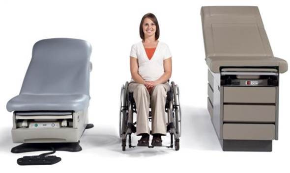 Fixed height examination table on right, adjustable height examination  table on left.  Woman in manual wheelchair positioned between the two tables.