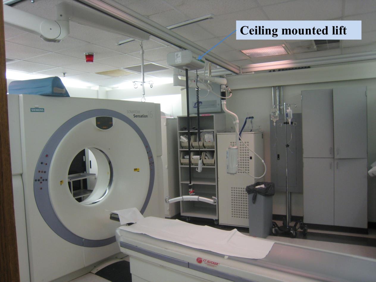 Photo of a CT room shown the CT equipment and an overhead lift mounted on the ceiling.