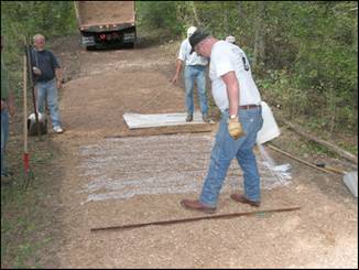 Figure 11---Treatment of wide bridle trail (site 2): spray application of Vitri-Turf in background and drip-bucket application of Soil-Sement in foreground. Note use of polyethylene-covered plywood for compaction and leveling of Vitri-Turf SEWF.