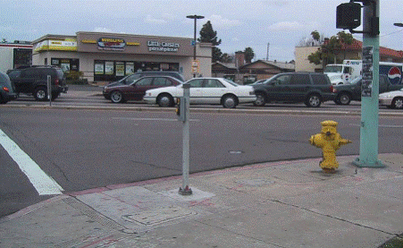 Photo from sidewalk looking across street with street parallel to photographer on left. Pole and fire hydrant are on right in photo. Additional small pole, about 4 feet high, is located near the crosswalk line, about 2 feet from the curb; APS is installed on that pole. 