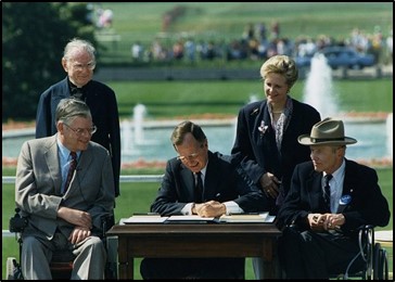 President Bush seated outside at a desk signing the ADA into law