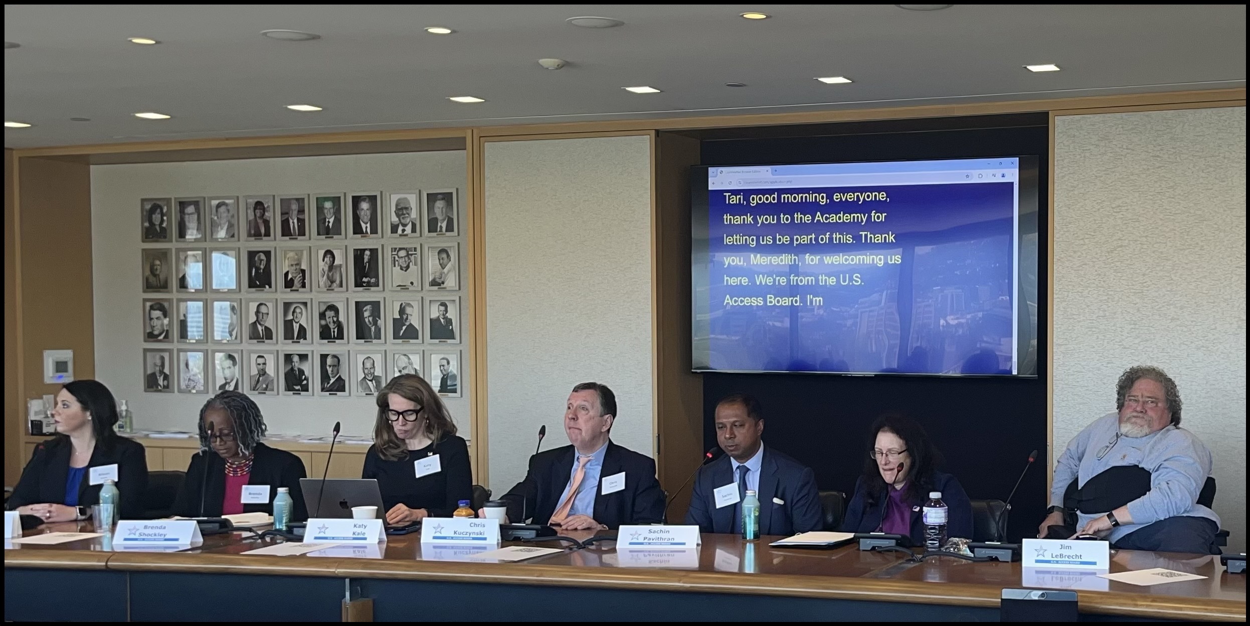 Access Board Members and staff sit at a large conference table. Behind them is a screen with the following caption: Tari, good morning, everyone, thank you to the Academy for letting us be part of this. Thank you, Meredith, for welcoming us here. We're from the U.S. Access Board.