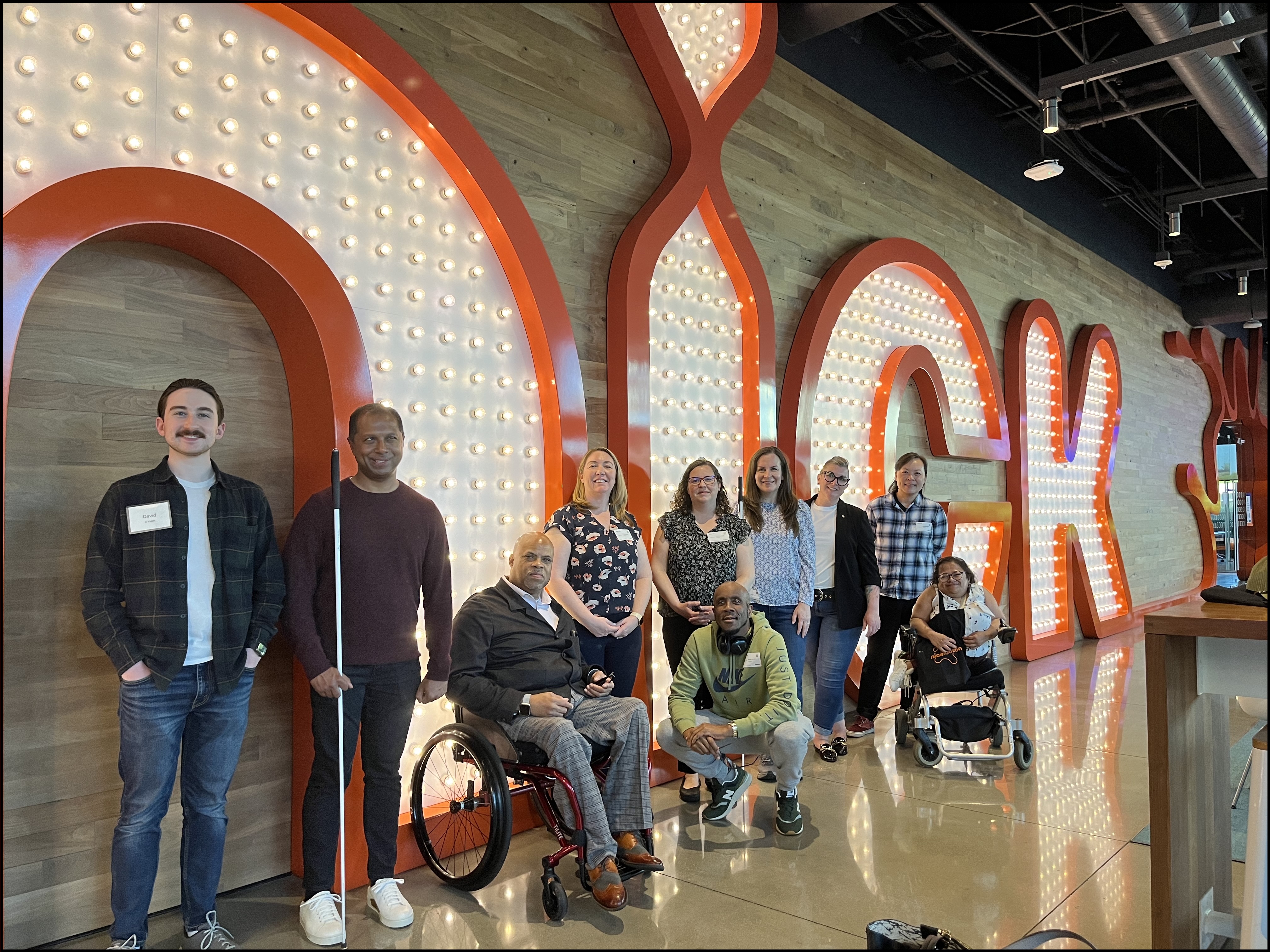 10 Access Board Members and staff pose in the lobby of Nickelodeon's Burbank studio. Behind them is a large neon sign that reads: nick.